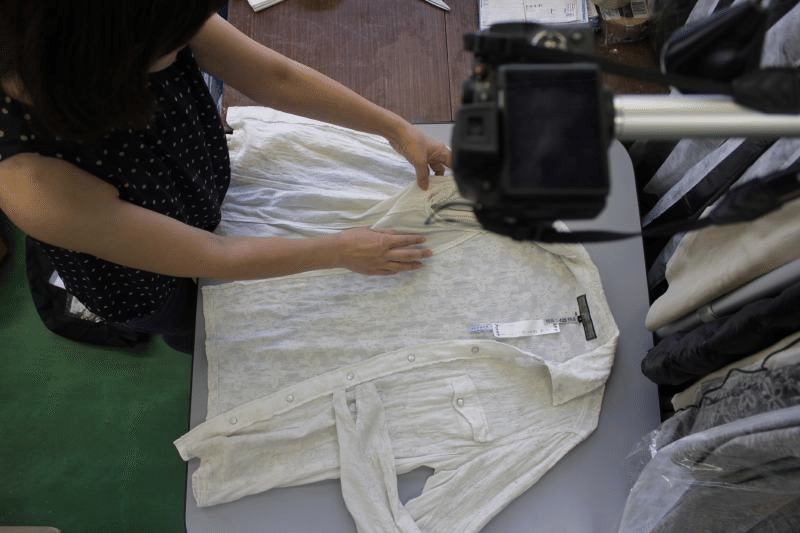 衣類の寸法や縫製を手で確かめる場面。一着ごとの状態を確認します。